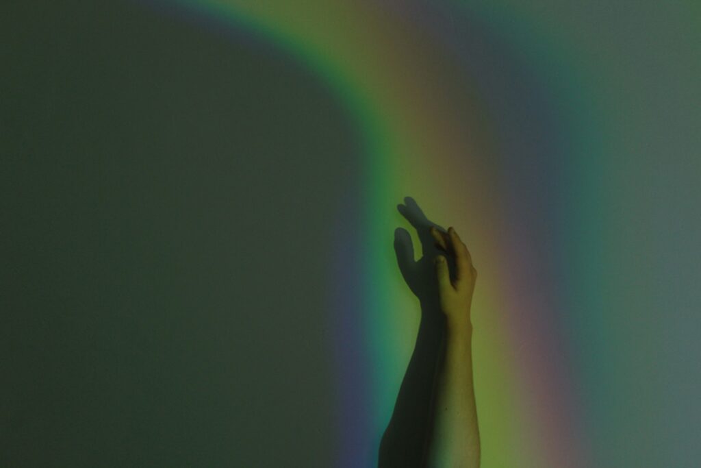 Eine Hand greift in einen Regenbogen aus Licht – queere Traumatherapie Berlin